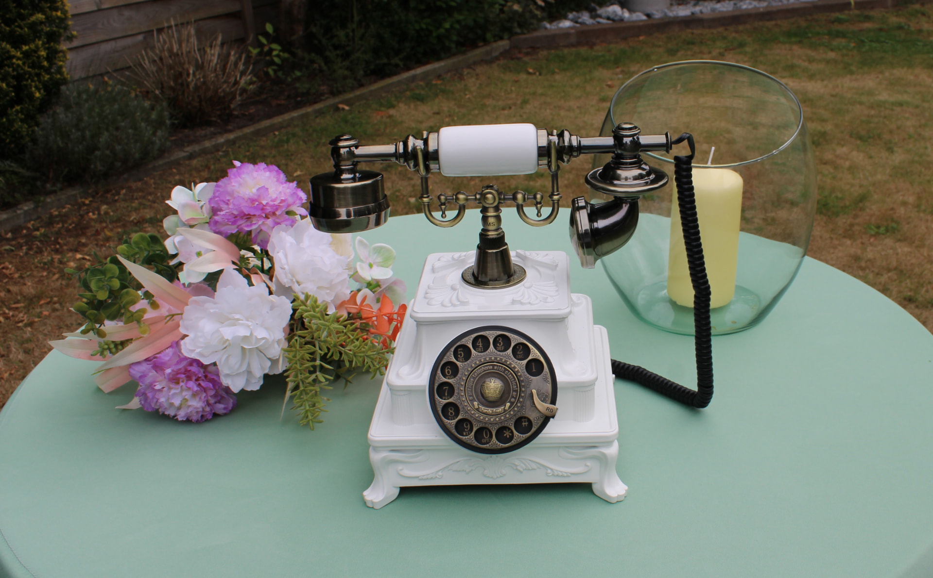 Witte luxe vintage telefoon met gouden details, bloemen en kaars op een tafel